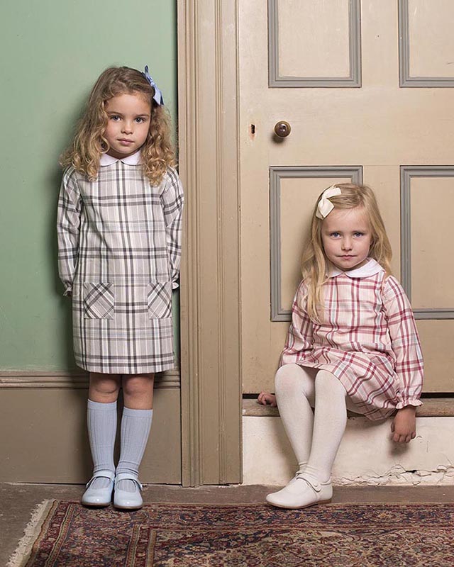 Photo of two little girls in similar dresses, one standing and one sitting on a doorstep.