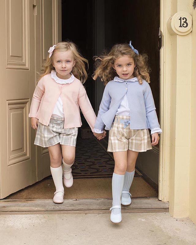 Two little girls wearing matching clothes stepping out hand-in-hand through a large old doorway