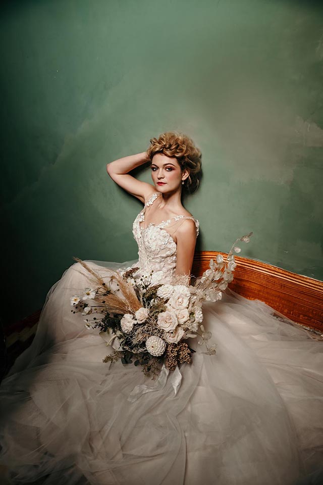 Woman reclining in bridal dress holding bouquet of dried flowers