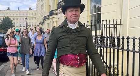 A man in Regency costume leading a tour group past a row of cream coloured town houses