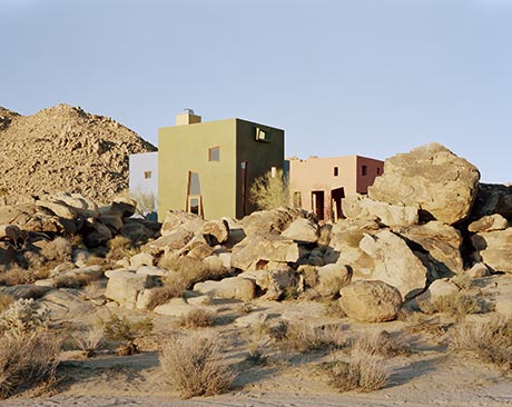 Photograph of three block-shaped buildings painted blue, green and orange, set in a rocky landscape