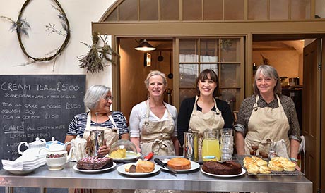 Photo of four women standing behind a table laden with cakes.