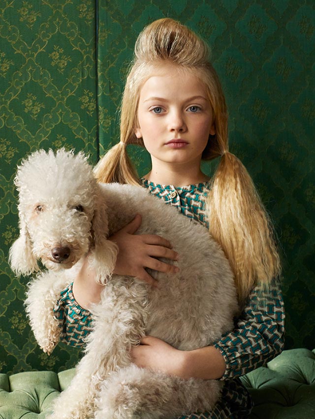 Photo of girl in a green dress holding a white Standard Poodle.