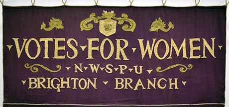 A photo of a large purple banner depicting: Votes for Women, N W S P U, Brighton Branch.