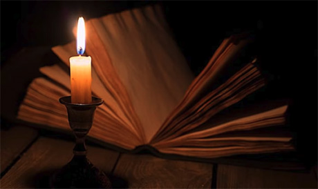Photograph of a lit candle in front of an open book
