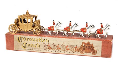 Photo of coronation coach toy. A gold coach pulled by eight white horses, arranged in pairs each pair with a rider in red costume.