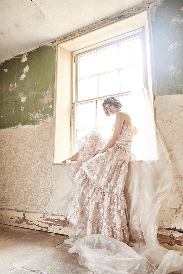 Young woman wearing long white gown, sitting on window ledge in derelict room