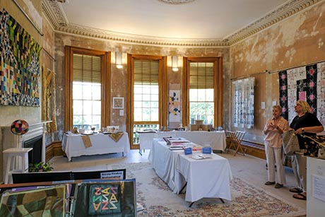 View of drawing room showing three tall windows, with artworks on the walls and displayed on tables.
