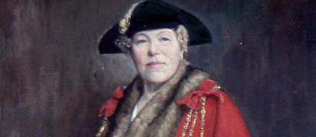 Painting of a lady wearing a red cloak, gold chains and a black cap.