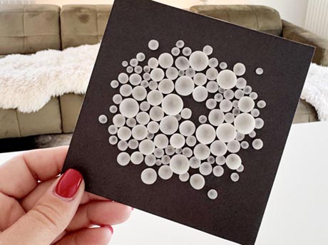 Photo of a hand holding a miniature artwork consisting of abstract white circles on a black background