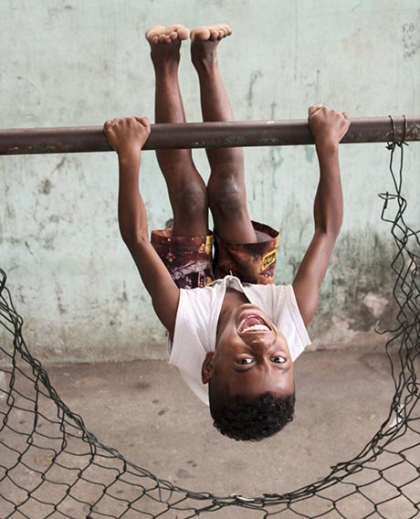 Photo of young boy, smiling happily at the camera while swinging upside down from a pipe.