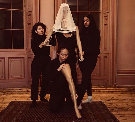 Photo: four women dressed in black, in rehearsal, one is veiled, one carries a mannequin leg.