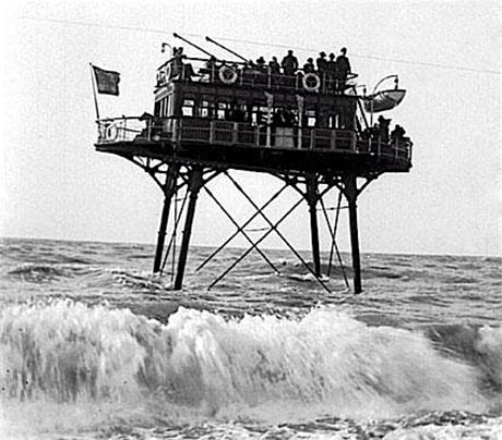 Photograph of Volk's 'Daddy Longlegs' electric railway. A two storey cabin on long metal legs trundling through the waves off Brighton beach.