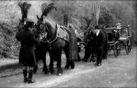 Black ad white photo of horse-drawn funeral procession. 
