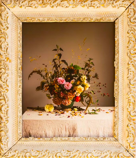 Photo of a flower arrangement contained within an ornate cream and gold frame 